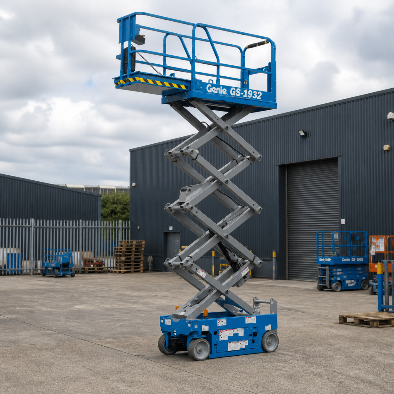 Genie scissor lift raised in the yard, with more platforms behind it.